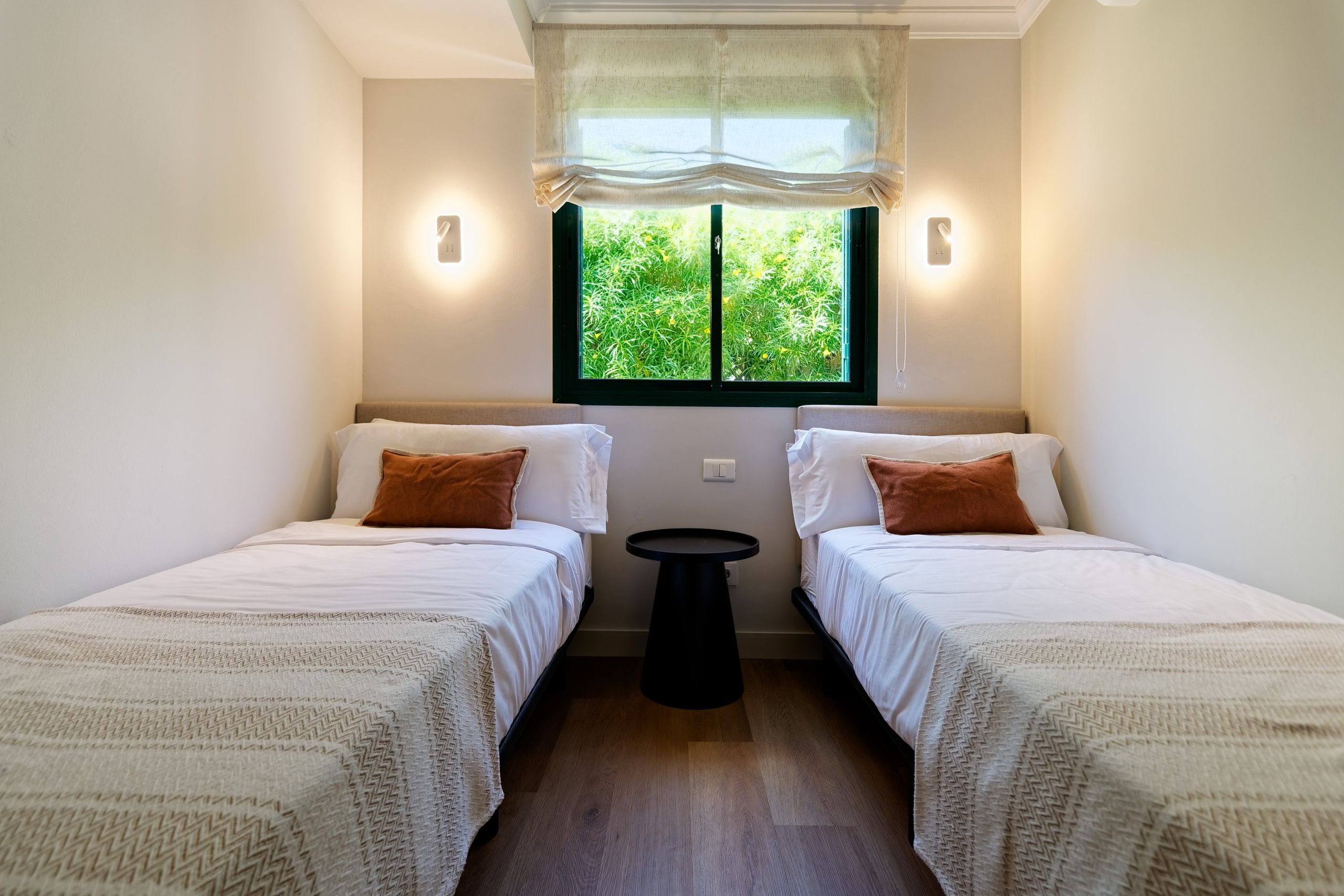 Une chambre avec deux lits, une fenêtre donnant sur un espace verdoyant et une petite table.