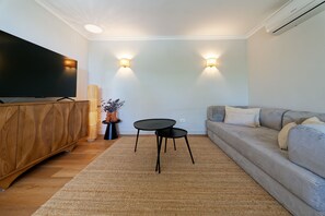 A modern living room with a flat-screen TV, a wooden cabinet, a round black table, a grey sofa, and two wall-mounted lamps. - Villa Catalina, just a short walk from the beach in San Agustín (San Bartolomé de Tirajana)