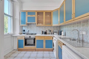 Uma cozinha moderna com forno embutido, micro-ondas e lava-louças, com armários em madeira clara e azul.