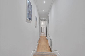 A hallway with a wooden floor, white walls, and a door at the end. - Bright 2B Apartment by the History Museum (Greater London)