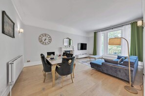A modern living room with a dining area, a sofa, a television, and a fireplace. - Bright 2B Apartment by the History Museum (Greater London)