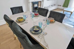 Mesa de jantar posta com pratos, copos e talheres, rodeada por cadeiras estofadas.
