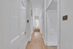 Ein Korridor mit weißen Türen, Holzdielen und einer Treppe, die zu einem anderen Raum führt.
