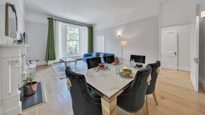 Ett modernt vardagsrum med en blå soffa, ett matbord med stolar och en öppen spis med en spegel.