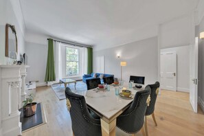Ein modernes Wohnzimmer mit einem blauen Sofa, einem Esstisch mit Stühlen und einem Kamin mit Spiegel.