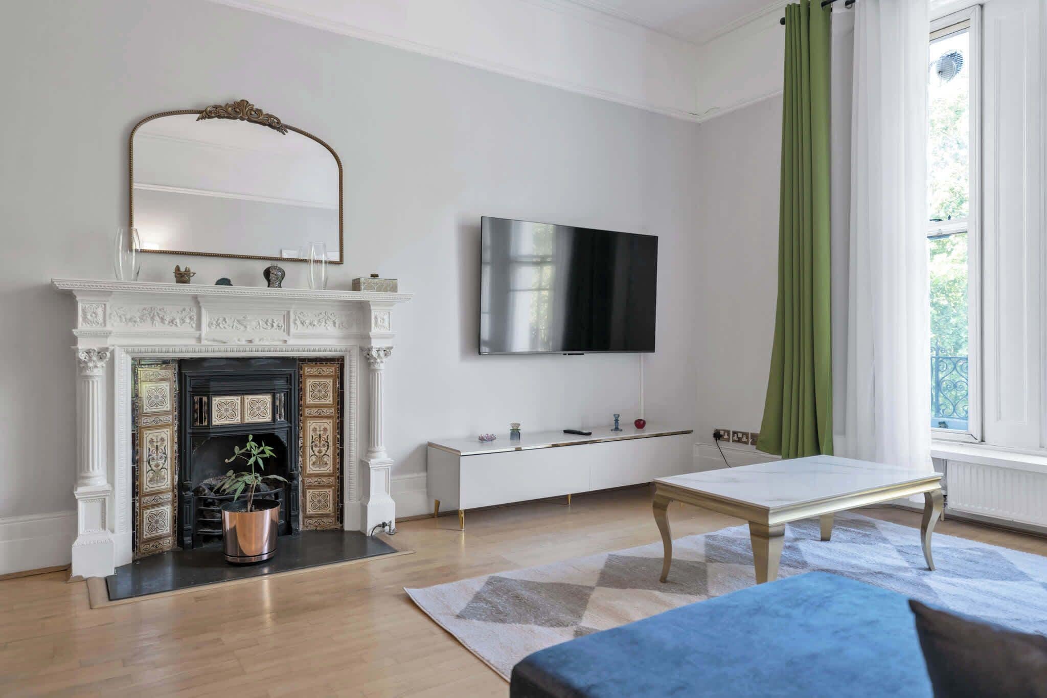 A modern living room with a fireplace, a flat-screen TV, a bench, and a window with curtains.