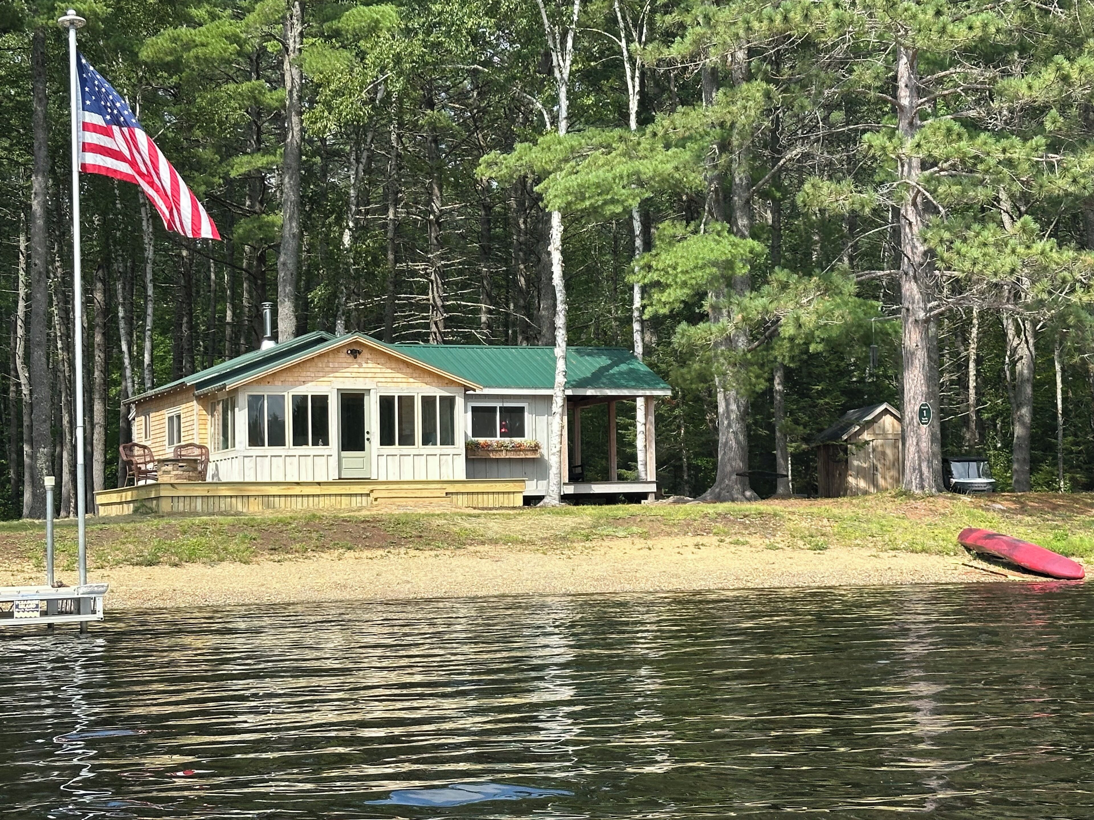 A cabin with a green roof, a dock, and an American flag.