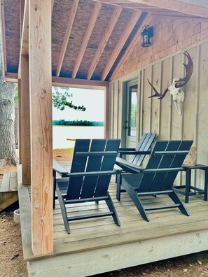 A wooden deck with Adirondack chairs, a wooden ceiling, and a mounted animal skull. - Private Island Cottage on Ebeemee Lake (Brownville)