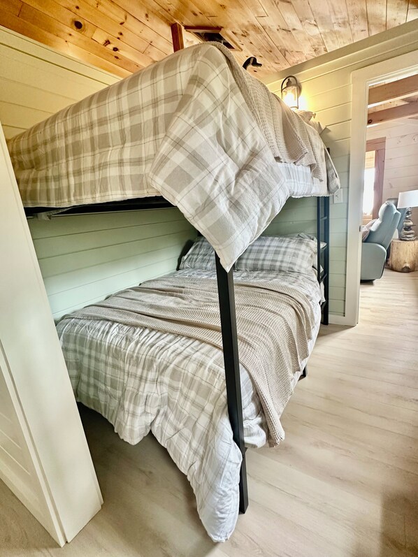 Una cama litera con una manta escocesa, suelo de madera y una lámpara en una mesita de noche.