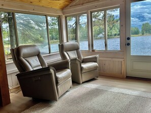 A room with two reclining chairs, large windows, a wooden ceiling, and a view of a lake. - Private Island Cottage on Ebeemee Lake (Brownville)