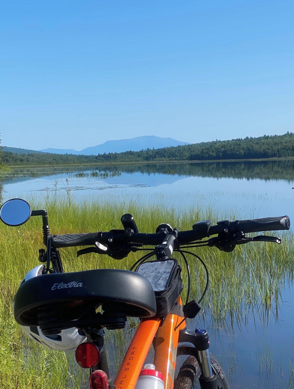 Un vélo avec une gourde et un sac, garé au bord d’un lac paisible, avec une colline boisée en arrière-plan.