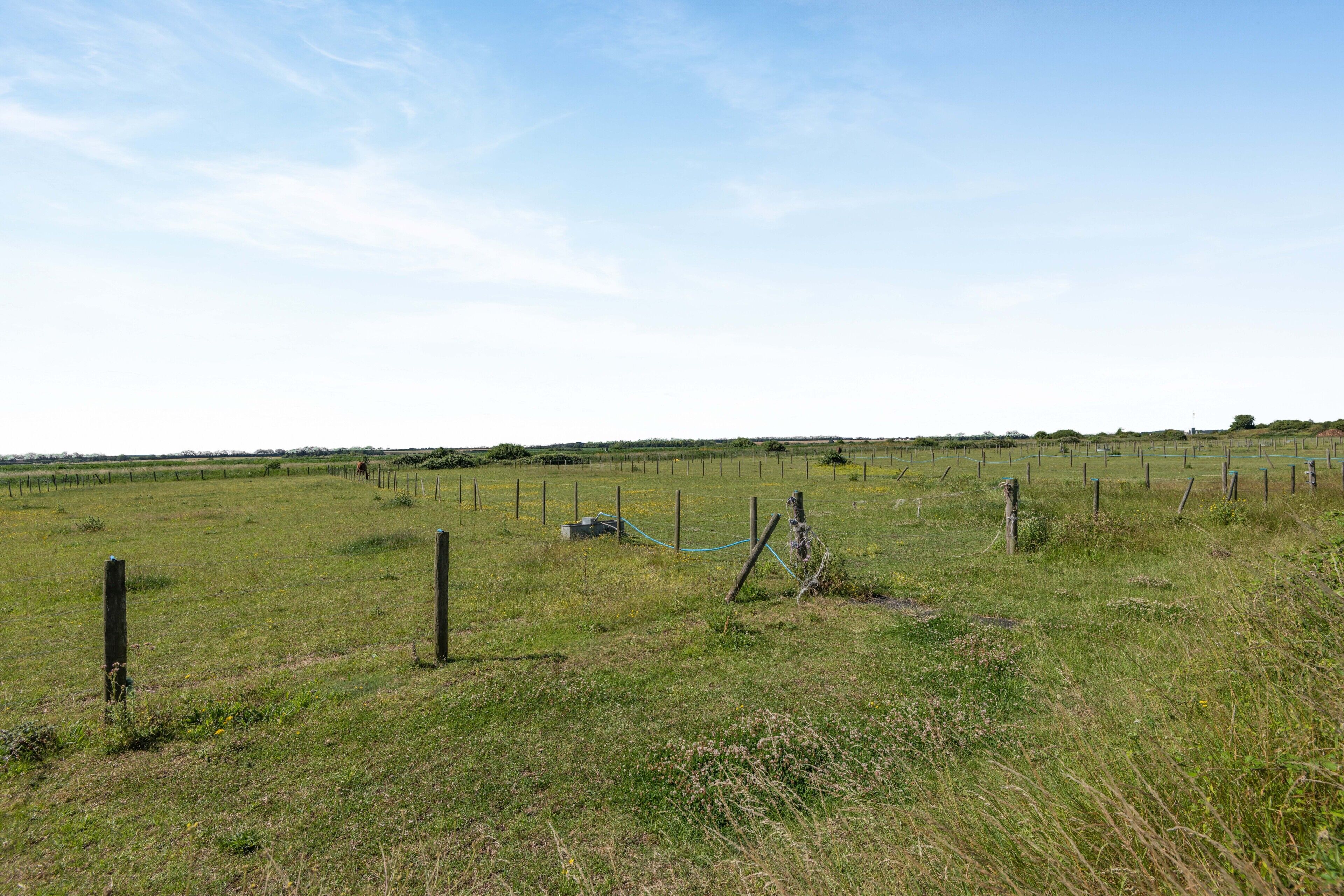 A rural landscape with a fenced field, a small structure, and a clear sky.