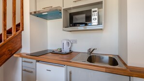 Una kitchenette compacta con microondas integrado, hervidor de agua y pileta de acero inoxidable.