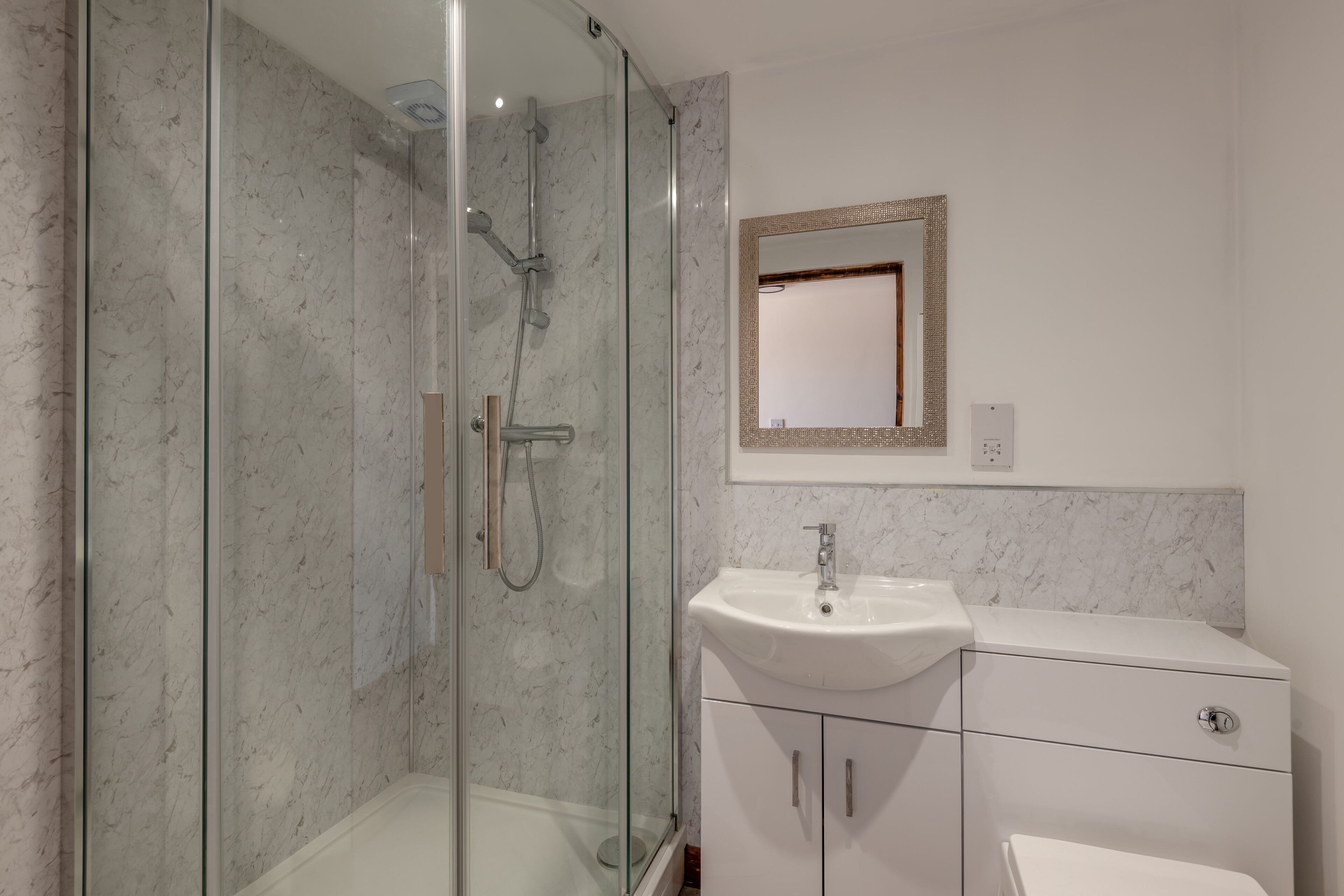 Un baño moderno con ducha de vidrio, un lavamanos blanco y un espejo con marco decorativo.