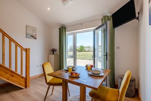 Un comedor con mesa de madera, sillas amarillas, una disposición para el desayuno y vistas a través de un ventanal.