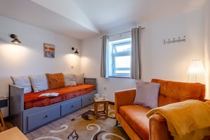 A modern living room with a sofa, a smaller couch, a table with a book and mugs, a window with curtains, and wall-mounted lights. - Kent Coast Stays (Birchington-on-Sea)