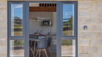 Puerta abierta que da a un comedor con una mesa, sillas y una cocina visible a través de la ventana.