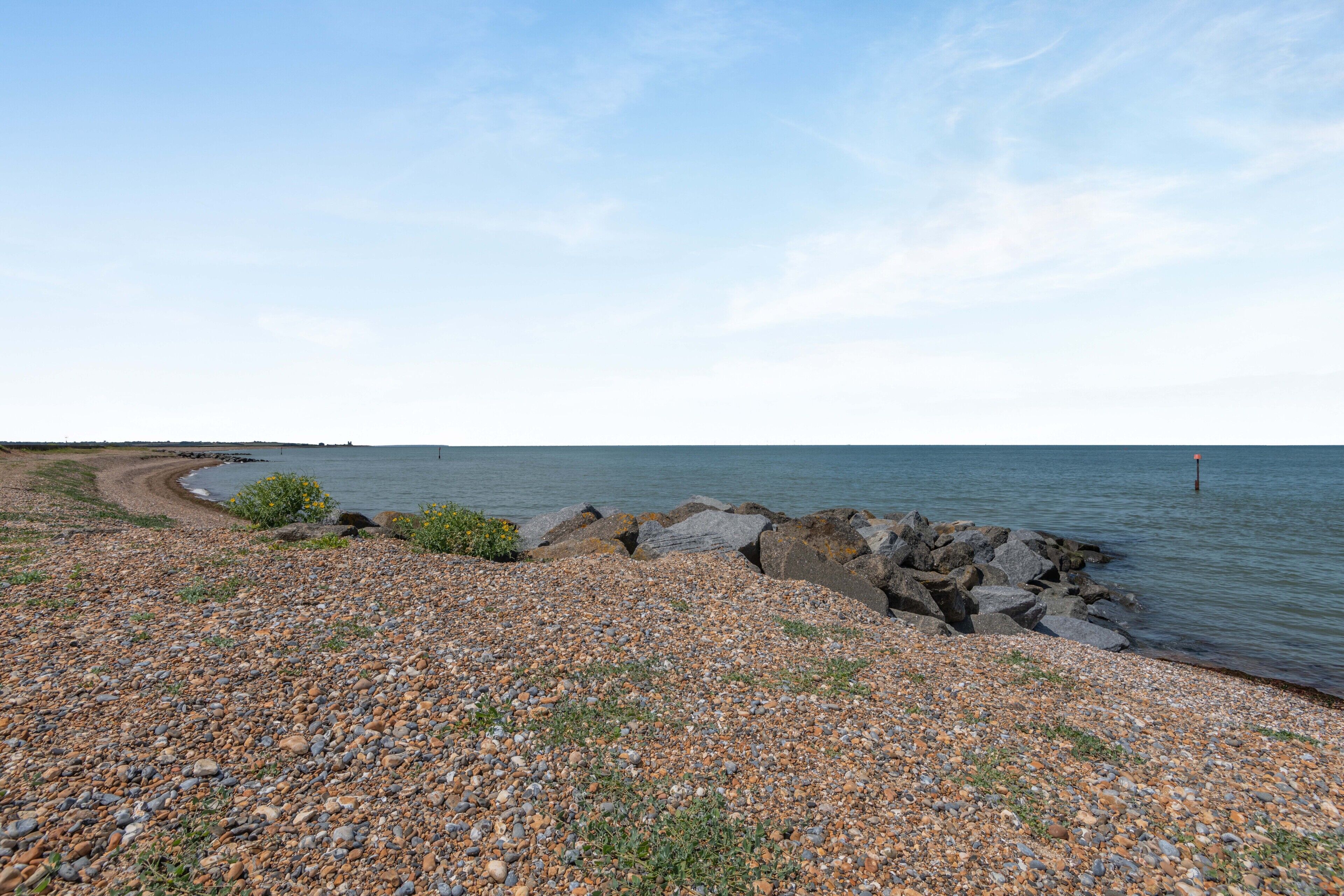 Une plage de galets bordée d’une côte rocheuse qui mène à une étendue d’eau calme.
