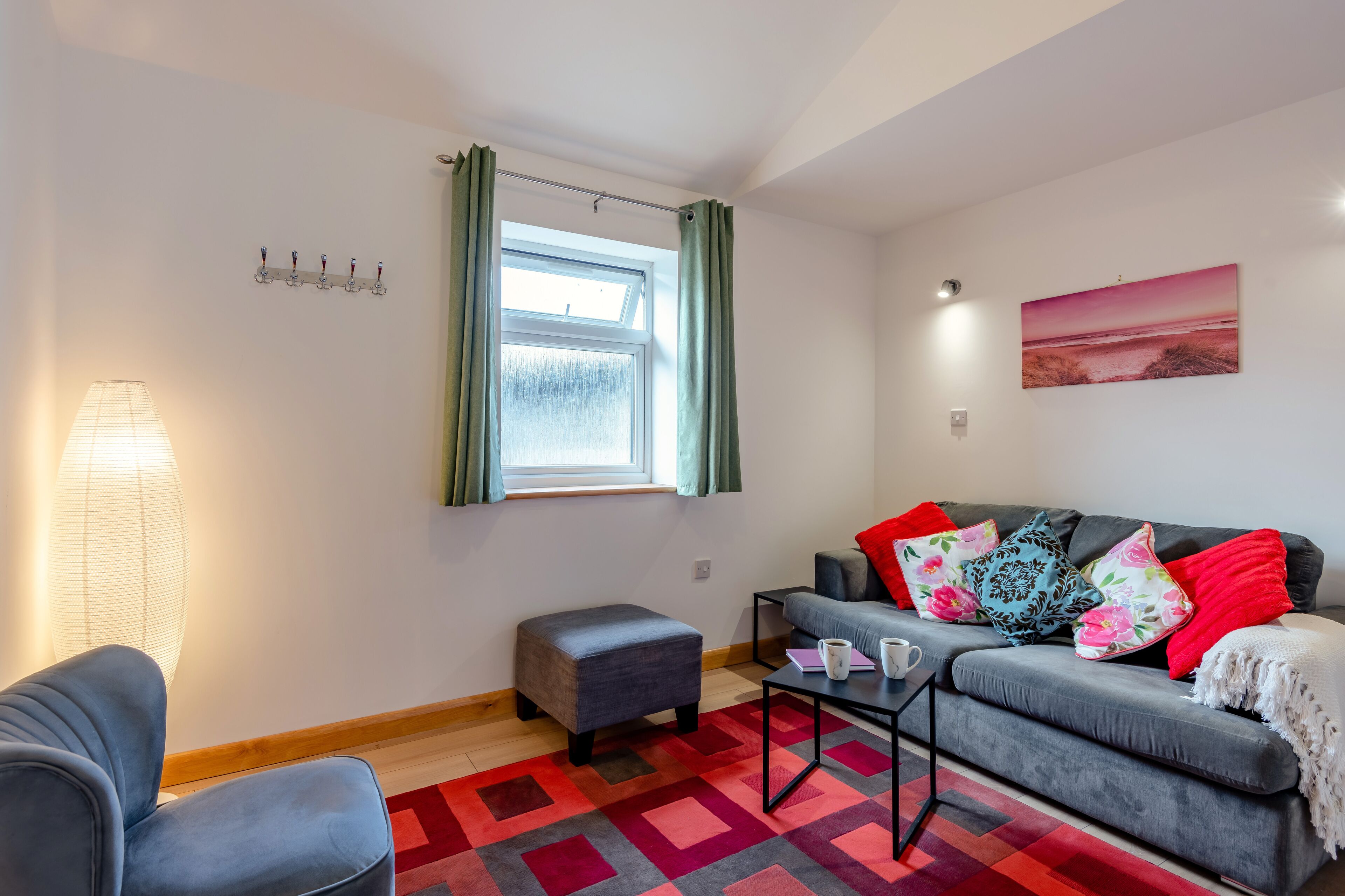 A modern living room with a grey sofa, a small ottoman, a coffee table, and a colorful rug.