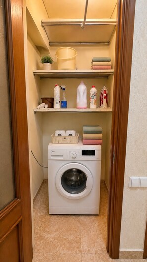 A laundry room with a washing machine, shelves with towels, and cleaning supplies. - Spacious 2BR Apartment with Balcony (Yerevan)
