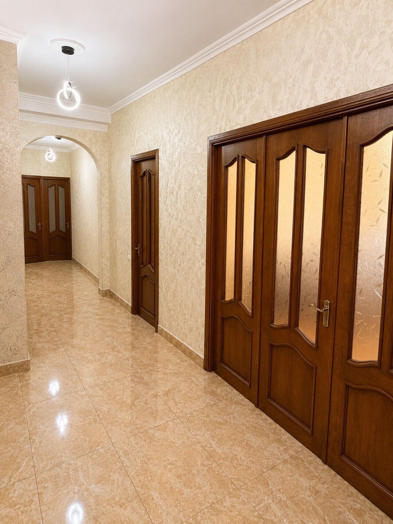 A hallway with a marble floor, wooden doors with glass panels, and a ceiling light fixture.