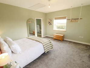A bedroom with a bed, a dresser, a mirror, a window, and a wall-mounted light fixture.