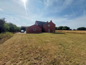 A red brick building with a sloped roof, a driveway, and a fenced field in the background. - Wold View (Market Rasen)