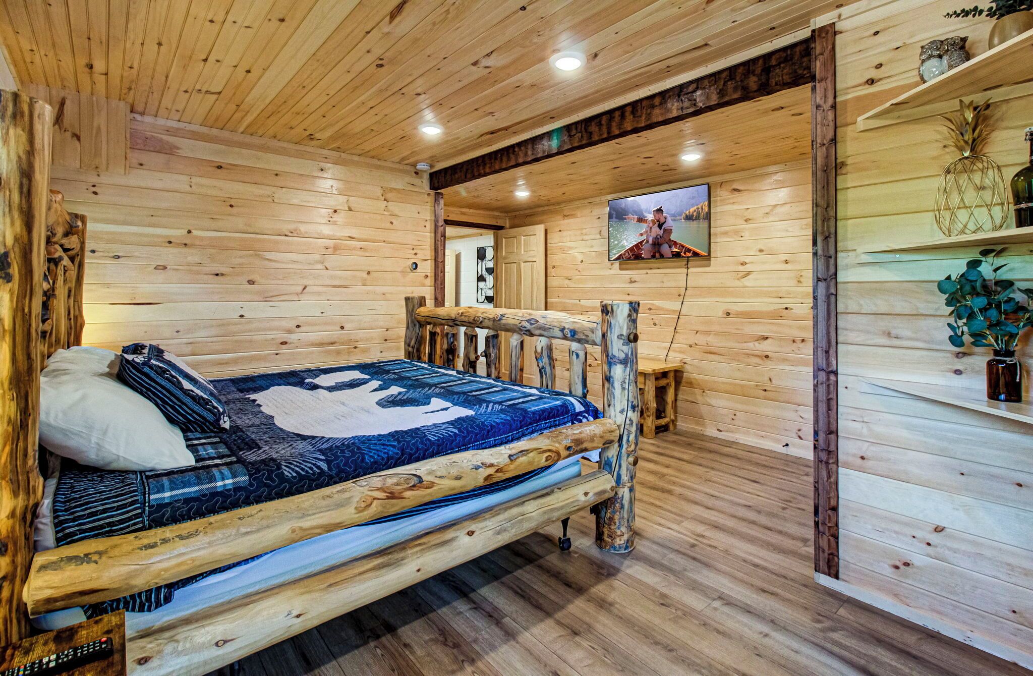 L’intérieur d’un chalet en bois comprend un lit, un téléviseur et une étagère ornée d’objets décoratifs.