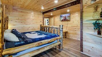L’intérieur d’un chalet en bois comprend un lit, un téléviseur et une étagère ornée d’objets décoratifs.
