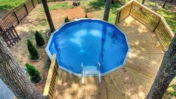 An octagonal above-ground swimming pool with a wooden deck, surrounded by trees and a wooden fence.