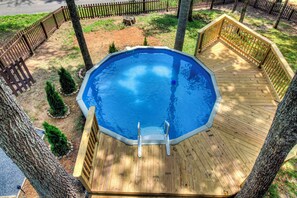 Une piscine hors sol octogonale, dotée d’une terrasse en bois et d’un escalier en métal, entourée d’arbres et d’une clôture en bois.