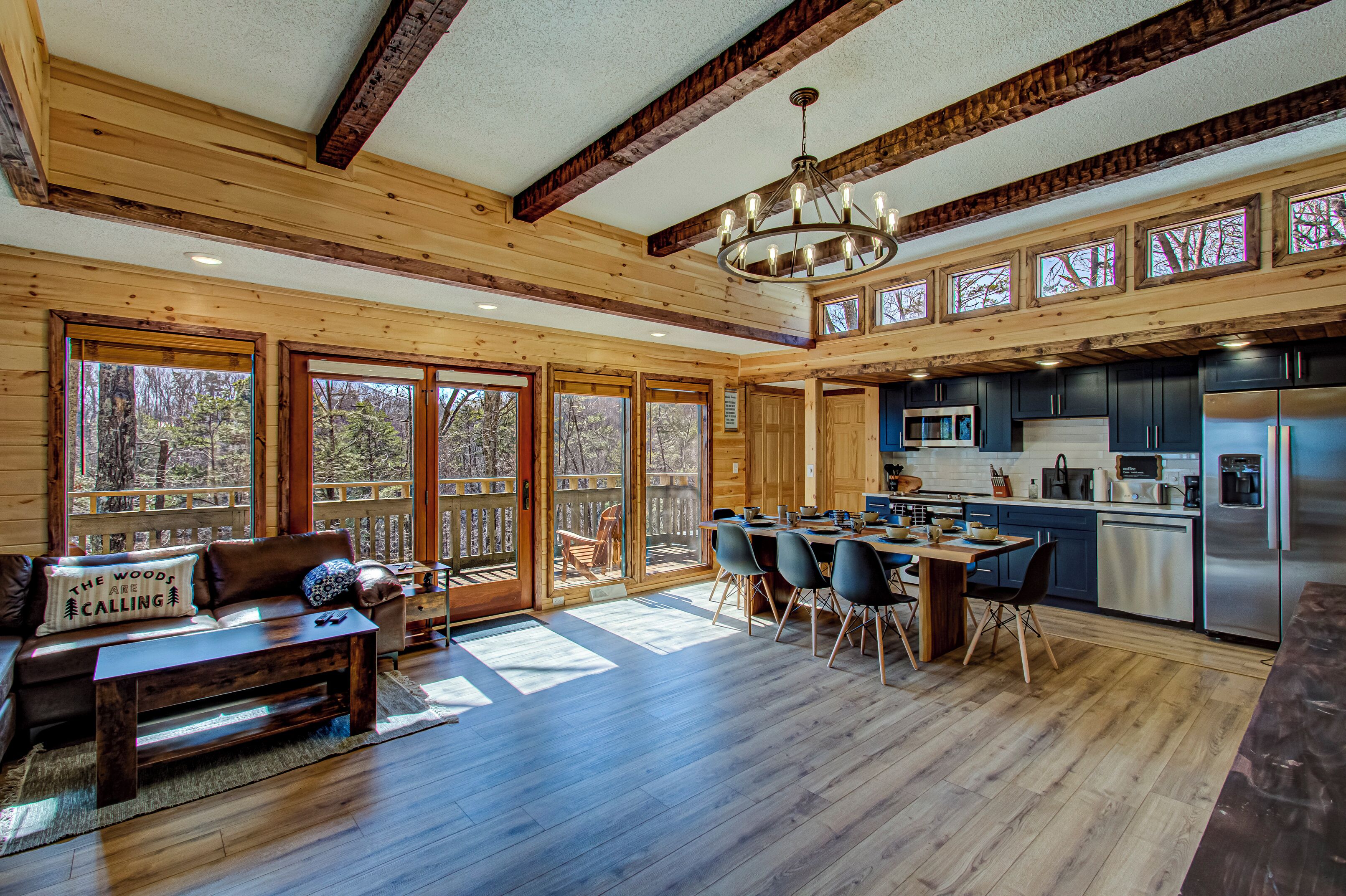A spacious cabin interior with a dining area, kitchen, and seating by large windows.