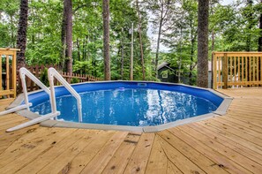 Une piscine extérieure dotée d’une terrasse en bois, entourée d’arbres.