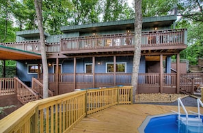 Une terrasse en bois à plusieurs niveaux, avec une piscine, le tout entouré d’arbres.