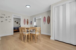 A dining area with a wooden table and chairs, a white door, and wall decorations including fish and surfboards. - Newly Renovated - Pet OK - 2BR Steps to Beach (Wildwood)