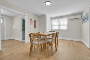 Un comedor con una mesa y sillas de madera, una ventana con persianas y un aire acondicionado instalado en la pared.