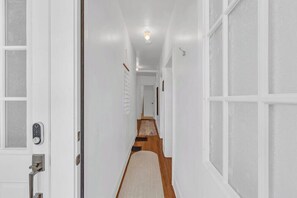 A narrow hallway with a wooden floor, white walls, and a door with a modern lock. - Zen Retreat in Asbury Park with Patio & Parking (Asbury Park)
