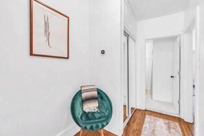 A hallway with a teal chair, a framed artwork, and a white door. - Zen Retreat in Asbury Park with Patio & Parking (Asbury Park)