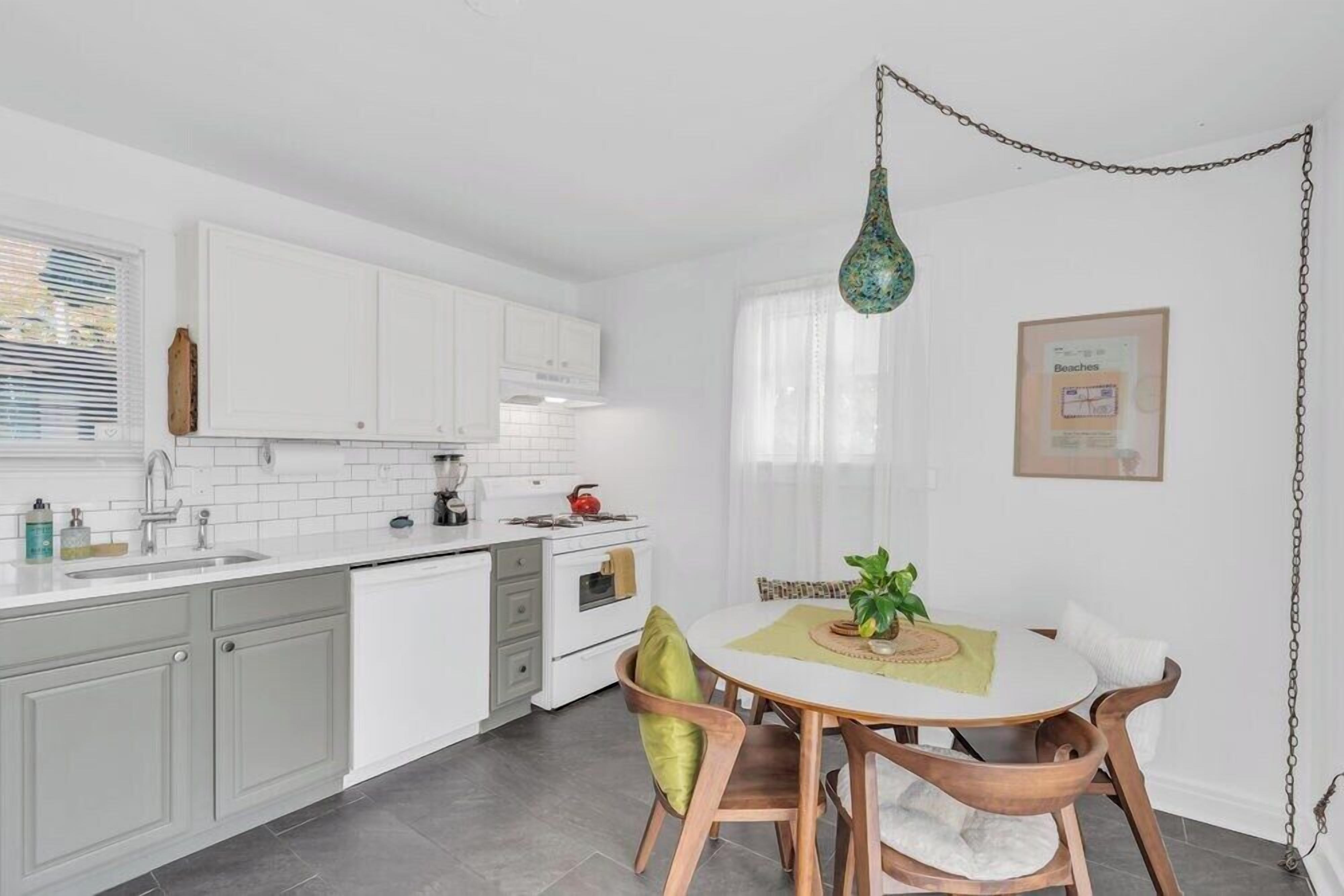 Une cuisine moderne avec des meubles blancs, une table à manger avec des chaises et un luminaire suspendu.