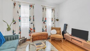 Ein Wohnzimmer mit einer Couch, einem Sessel, einem Couchtisch mit Büchern, einem Fernseher und einer Gitarre.