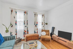 A living room with a sofa, a chair, a coffee table with books, a television, and a guitar. - Zen Retreat in Asbury Park with Patio & Parking (Asbury Park)