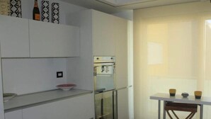 Una cocina con armarios blancos, un horno con puerta de vidrio y una mesa pequeña con tazas.