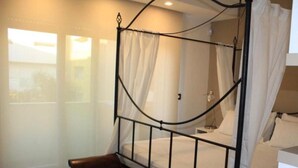 Quarto com cama de dossel, um banco e janela com cortinas.
