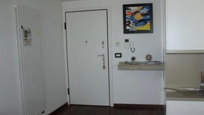 Um quarto com porta branca, radiador, uma pequena prateleira com objetos decorativos e um quadro na parede.