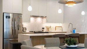 Una cocina moderna con electrodomésticos de acero inoxidable, una isla central con asientos, iluminación colgante y un cesto de basura visible.