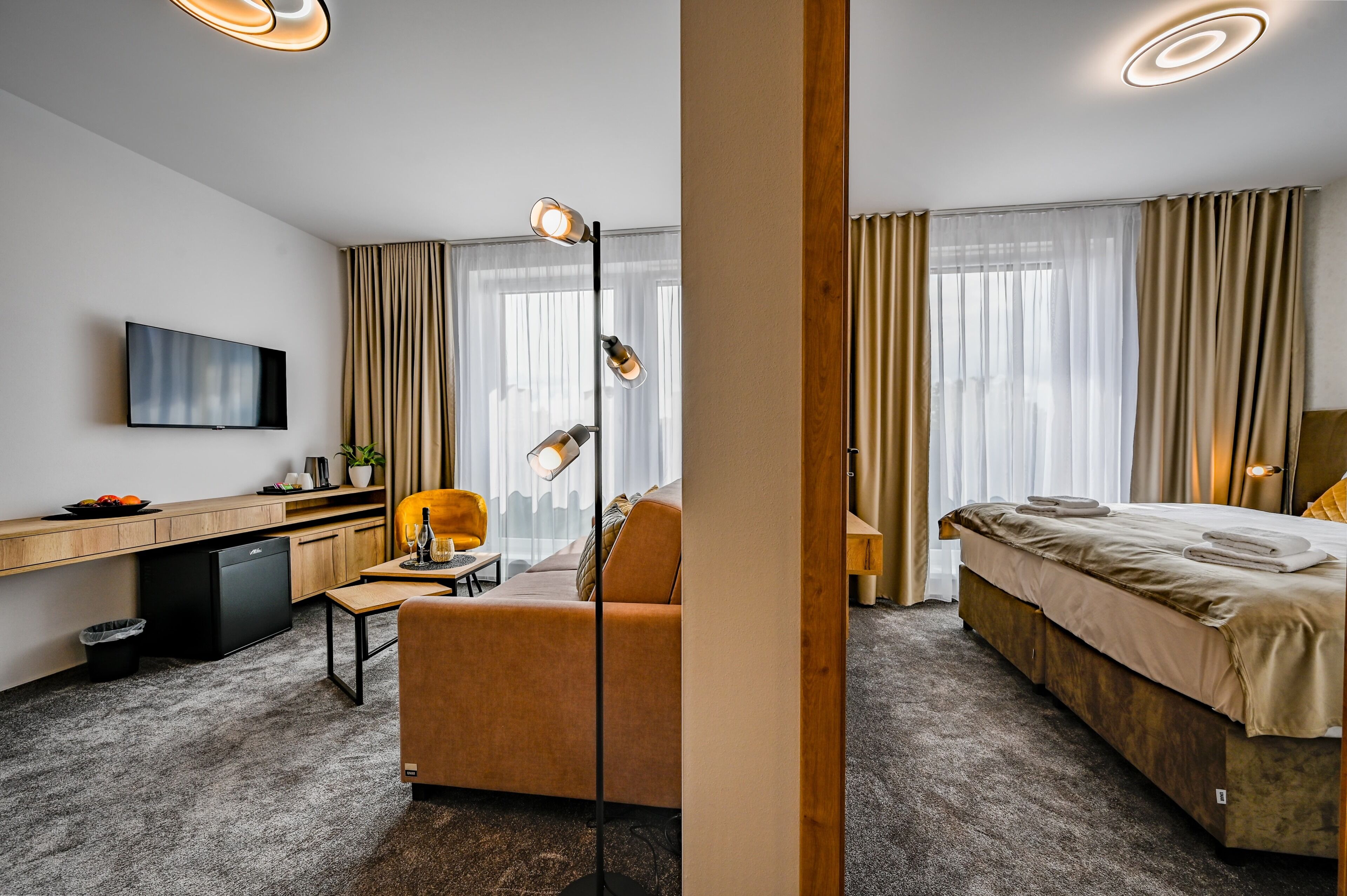 Ein Hotelzimmer mit Bett, Schreibtisch, Stuhl, Fernseher und einem Fenster mit Vorhängen.