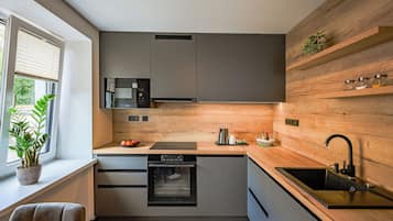 Cocina moderna con armarios grises, horno empotrado, microondas y una pared de acento de madera.