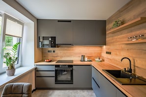 A modern kitchen with grey cabinets, a built-in oven, a microwave, and a wooden accent wall. - Penzión u Jakuba (Martin)
