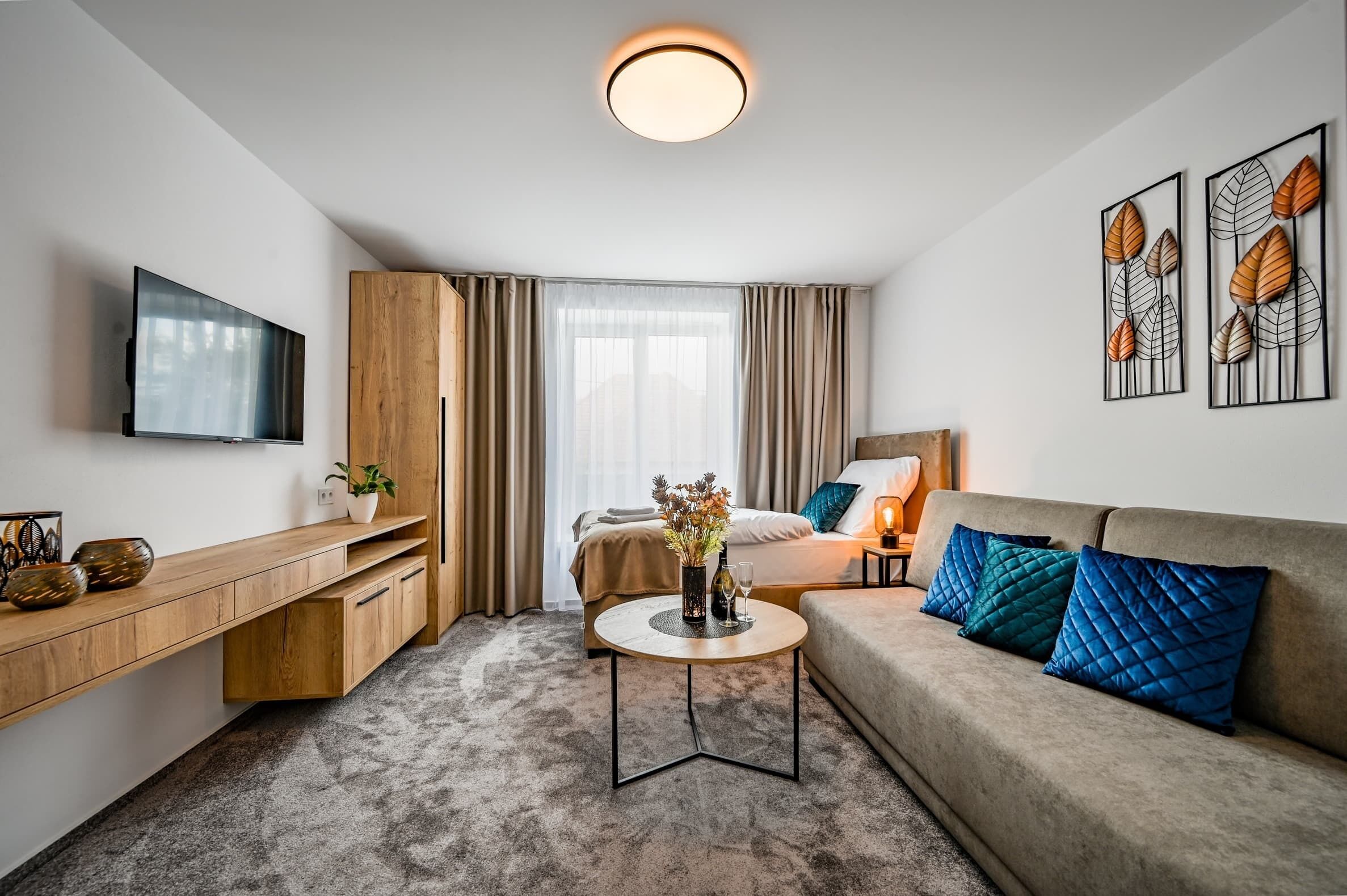 Ein modernes Hotelzimmer mit einem Flachbildfernseher, einem Holztisch, einem runden Couchtisch, einer blauen Sitzsofa und Kunstwerken an den Wänden.