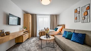Ein modernes Hotelzimmer mit einem Flachbildfernseher, einem Holztisch, einem runden Couchtisch, einer blauen Sitzsofa und Kunstwerken an den Wänden.